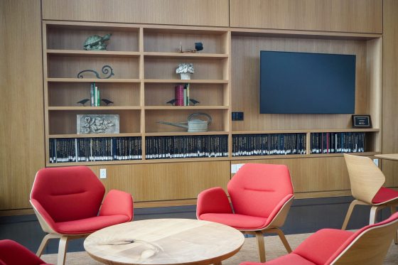 A library setting featuring red chairs, wood tables, and shelving with a variety of display items.